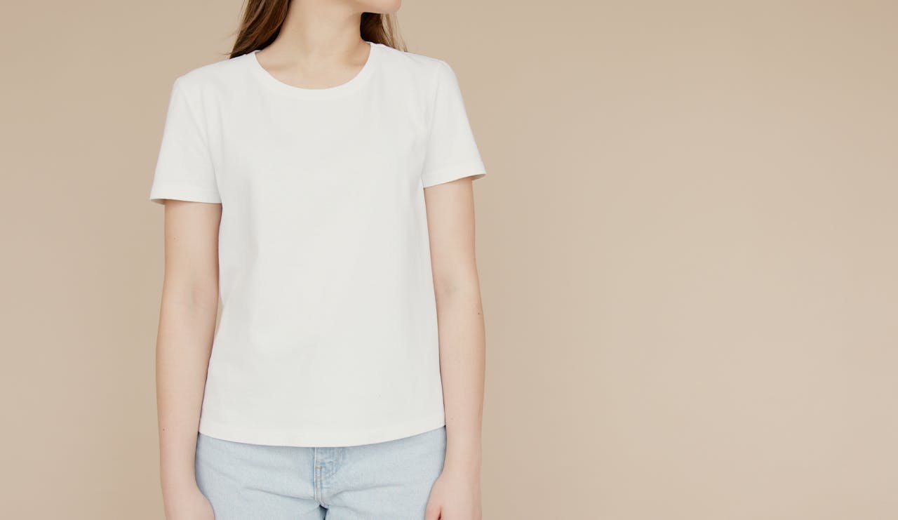 Mockup of a woman in a white t-shirt and jeans on a beige background, ideal for fashion branding.